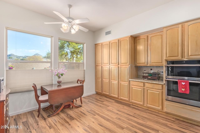 kitchen with decorative backsplash, light stone countertops, light wood-type flooring, light brown cabinetry, and stainless steel double oven