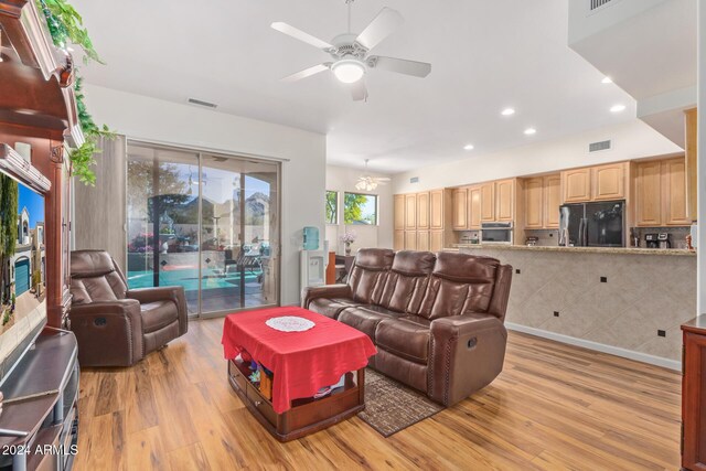 living room with light hardwood / wood-style floors and ceiling fan with notable chandelier