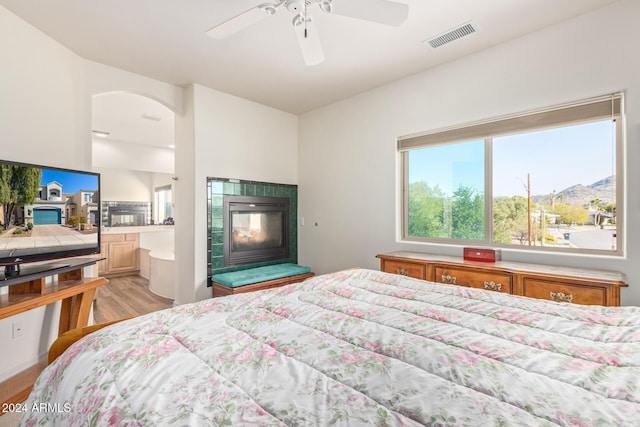 bedroom featuring ensuite bathroom, a fireplace, ceiling fan, a mountain view, and light hardwood / wood-style floors