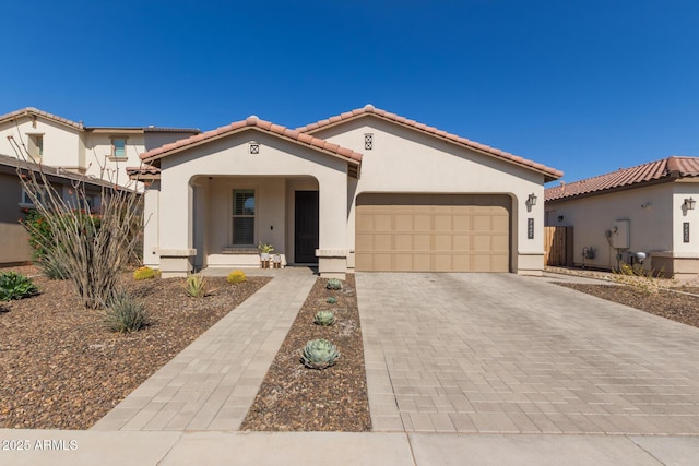 mediterranean / spanish-style home featuring a garage, decorative driveway, a tile roof, and stucco siding