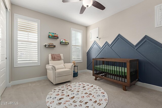 bedroom with a crib, a ceiling fan, light colored carpet, and baseboards