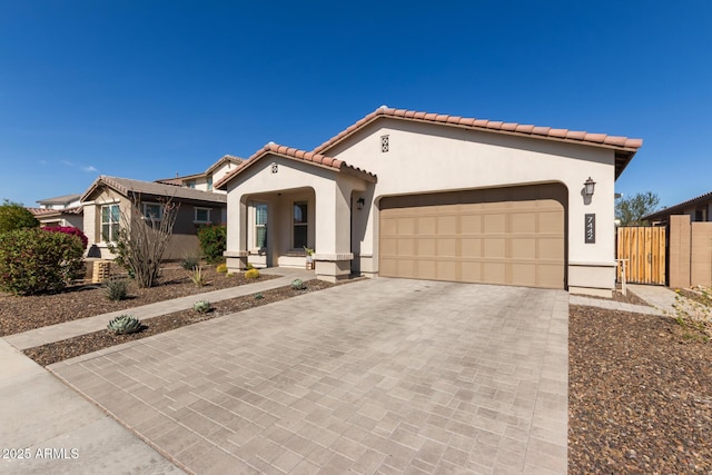 mediterranean / spanish house with a garage, fence, a tiled roof, decorative driveway, and stucco siding