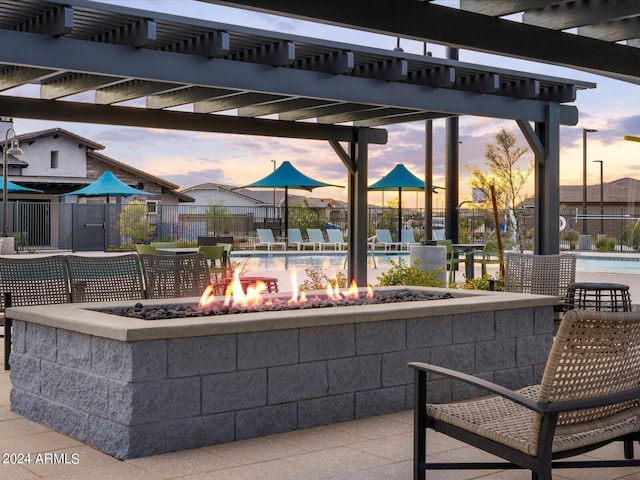 patio terrace at dusk with a community pool, a pergola, and an outdoor fire pit