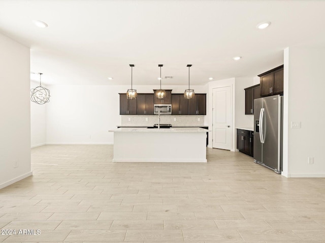 kitchen featuring backsplash, appliances with stainless steel finishes, decorative light fixtures, and a center island with sink