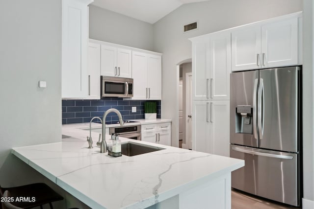 1057 W Laurel Ave, Gilbert, AZ 85233 - kitchen featuring stainless steel appliances, a peninsula, backsplash, light stone counters, and arched walkways