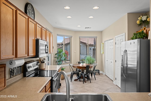 kitchen with light tile patterned floors, a sink, visible vents, appliances with stainless steel finishes, and brown cabinetry