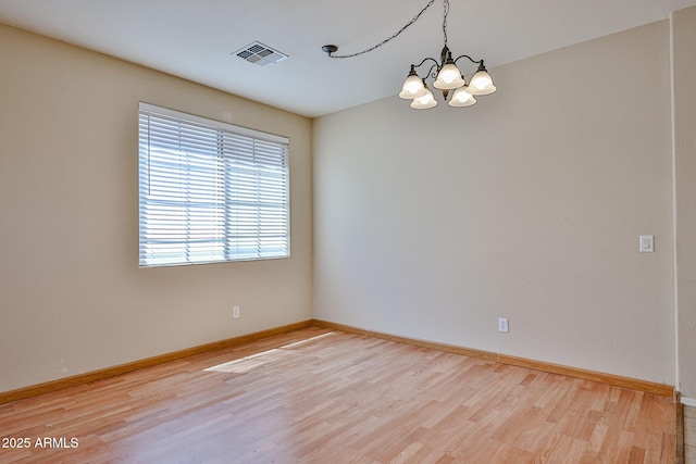 empty room with an inviting chandelier, visible vents, wood finished floors, and baseboards