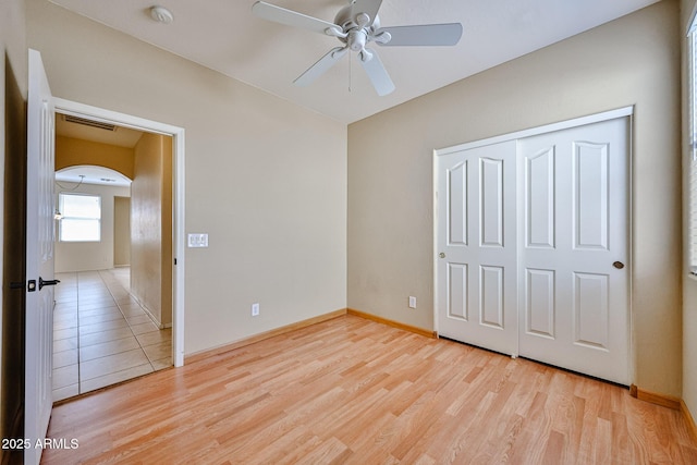 unfurnished bedroom featuring light wood-type flooring, a closet, baseboards, and arched walkways