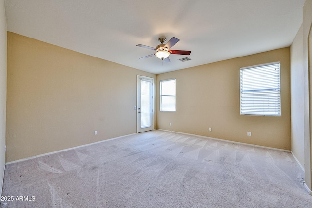 empty room featuring a ceiling fan, visible vents, light carpet, and baseboards
