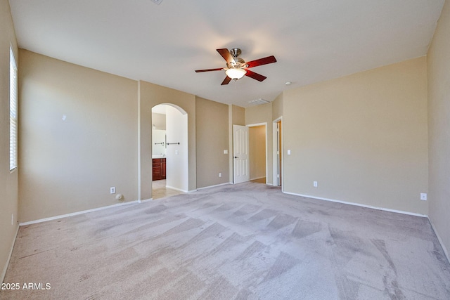 unfurnished bedroom with connected bathroom, light carpet, baseboards, and arched walkways