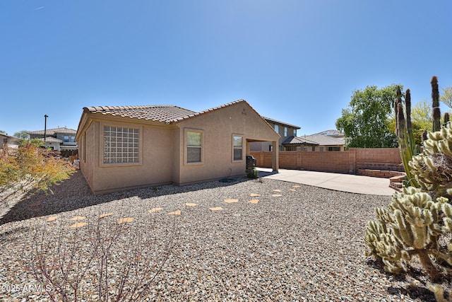 rear view of house featuring stucco siding, a tiled roof, a patio area, and a fenced backyard