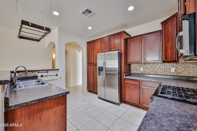 kitchen with arched walkways, appliances with stainless steel finishes, dark countertops, a sink, and visible vents