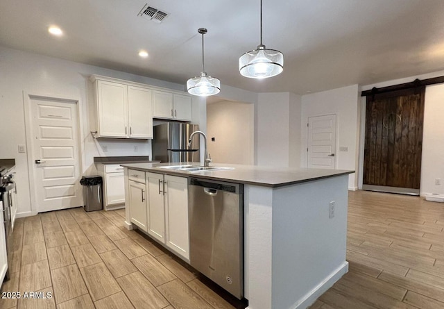 kitchen featuring visible vents, a center island with sink, a sink, stainless steel appliances, and white cabinets