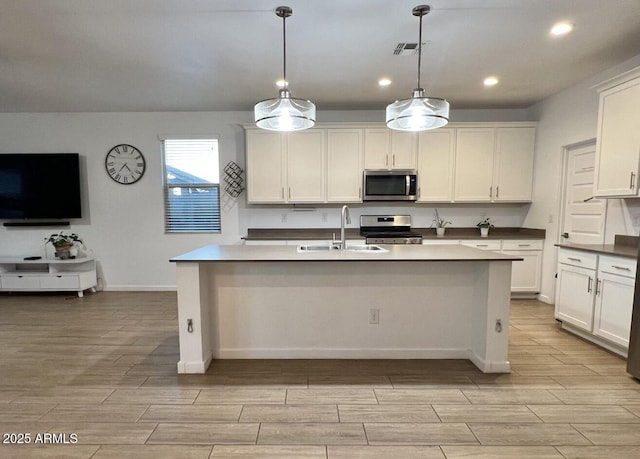 kitchen featuring wood finish floors, a kitchen island with sink, a sink, recessed lighting, and stainless steel appliances