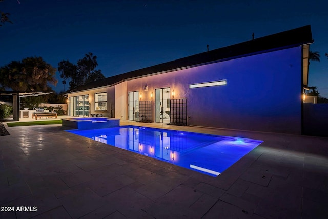 pool at twilight featuring a pool with connected hot tub, a patio, and area for grilling