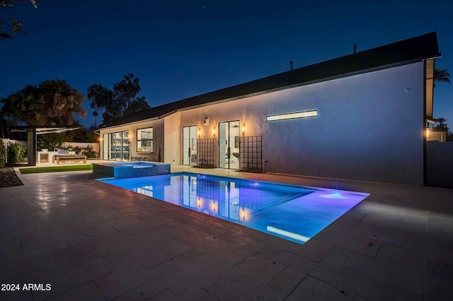 pool at twilight with a pool with connected hot tub, an outdoor kitchen, and a patio