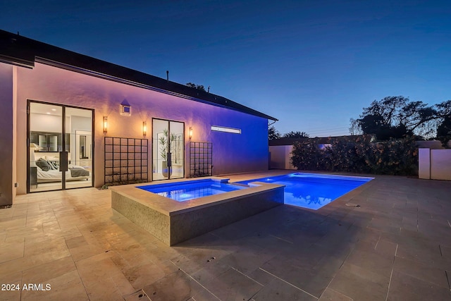 pool at dusk with an in ground hot tub and a patio area