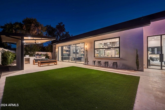 back of house at twilight with a patio, a lawn, and stucco siding