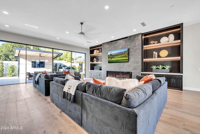 living area with recessed lighting, a large fireplace, a ceiling fan, built in features, and light wood finished floors