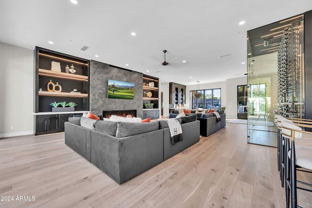 living room with built in shelves, recessed lighting, a large fireplace, visible vents, and light wood-style floors