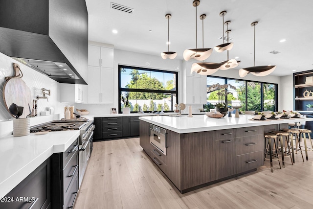 kitchen with light hardwood / wood-style flooring, wall chimney range hood, a wealth of natural light, and white cabinets