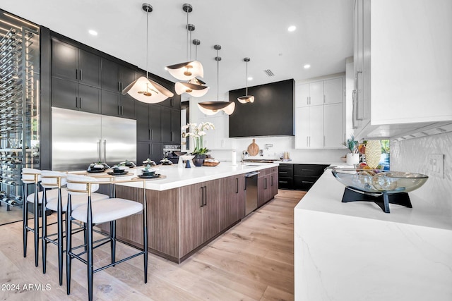 kitchen featuring stainless steel appliances, hanging light fixtures, light wood-type flooring, a large island with sink, and a kitchen breakfast bar