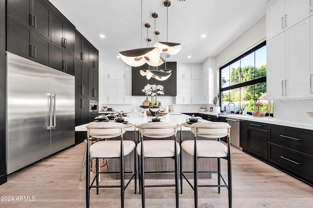 kitchen with a kitchen island, hanging light fixtures, light hardwood / wood-style floors, stainless steel appliances, and white cabinets