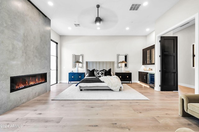 bedroom featuring a tile fireplace, light wood-type flooring, and ceiling fan