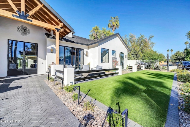 rear view of house featuring a patio area, a yard, and stucco siding