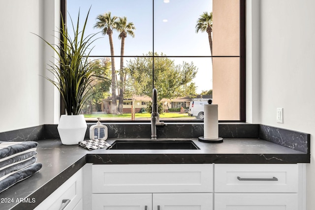 kitchen with dark countertops, white cabinetry, and a sink