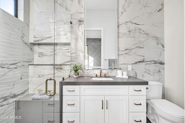 bathroom featuring vanity, walk in shower, toilet, and tile walls