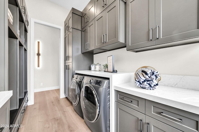 laundry area featuring baseboards, cabinet space, light wood-style flooring, and washing machine and clothes dryer