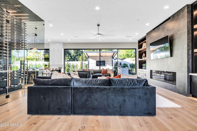 living area with built in shelves, recessed lighting, a large fireplace, and light wood-style flooring