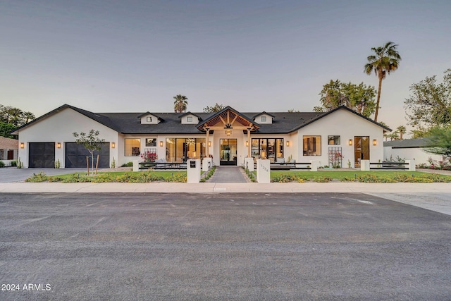 modern farmhouse featuring a garage, driveway, a fenced front yard, french doors, and stucco siding