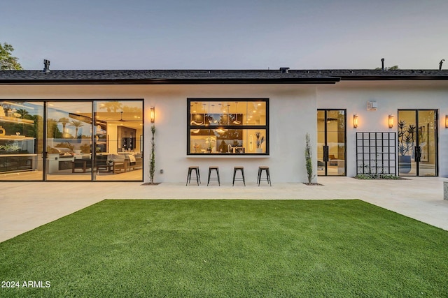 back house at dusk featuring a patio area and a lawn