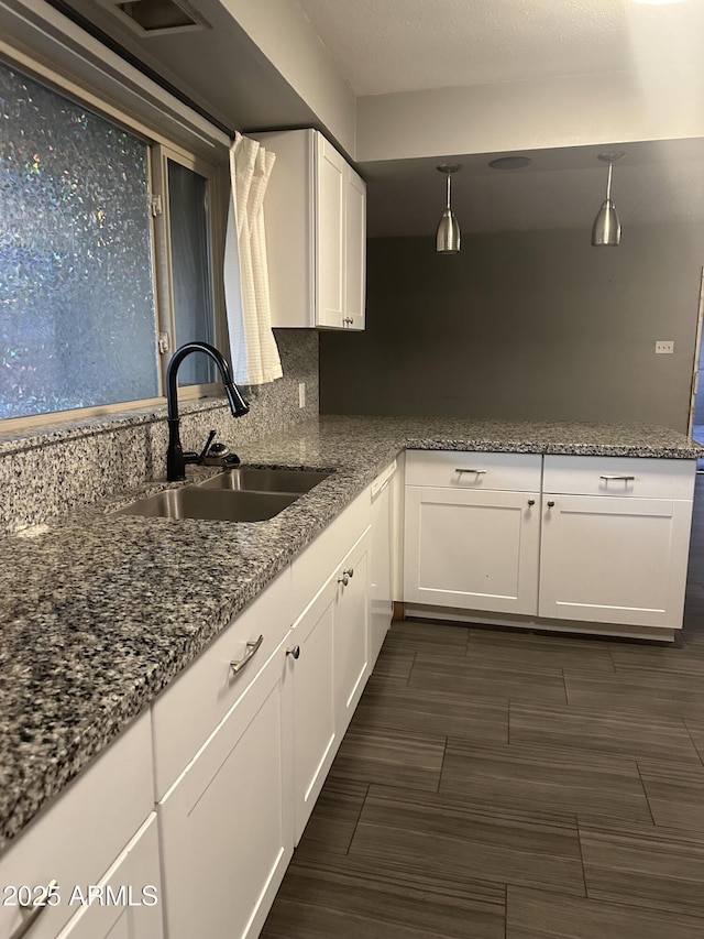 kitchen featuring hanging light fixtures, sink, dark stone countertops, and white cabinets