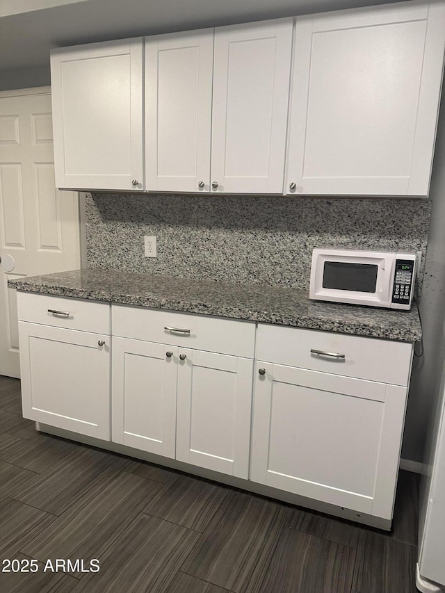 kitchen featuring white cabinetry, dark stone counters, dark hardwood / wood-style floors, and decorative backsplash