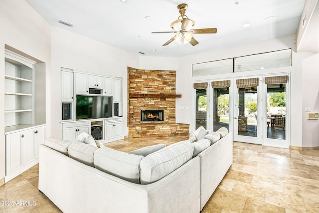 living room featuring a stone fireplace, a ceiling fan, and visible vents