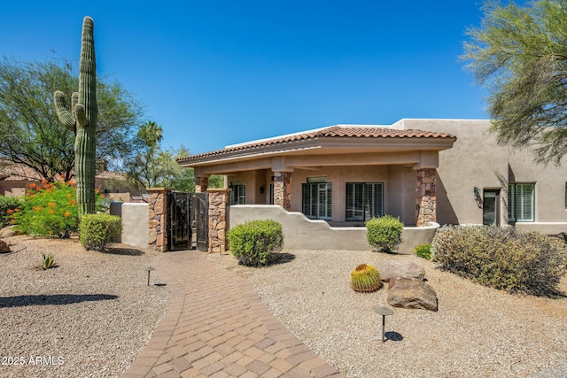 back of house featuring stone siding, stucco siding, a tile roof, and a gate