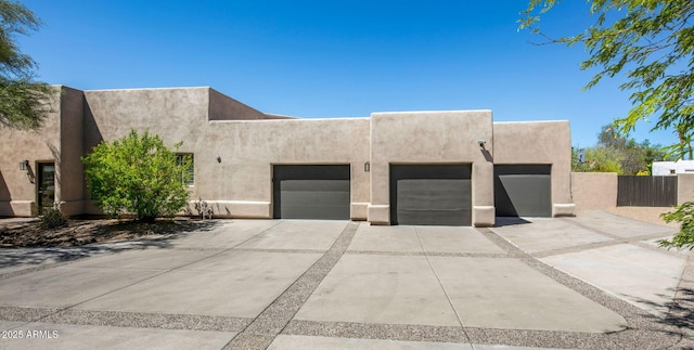 pueblo-style house with stucco siding, driveway, an attached garage, and fence