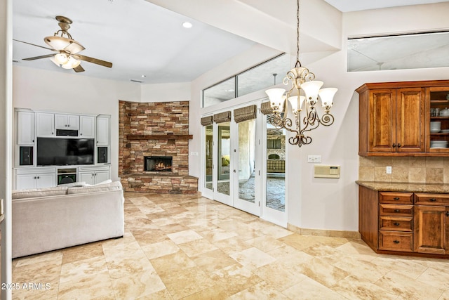 kitchen featuring light stone counters, brown cabinets, open floor plan, ceiling fan with notable chandelier, and tasteful backsplash