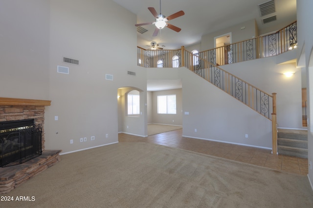 unfurnished living room featuring a fireplace, light carpet, a towering ceiling, and ceiling fan