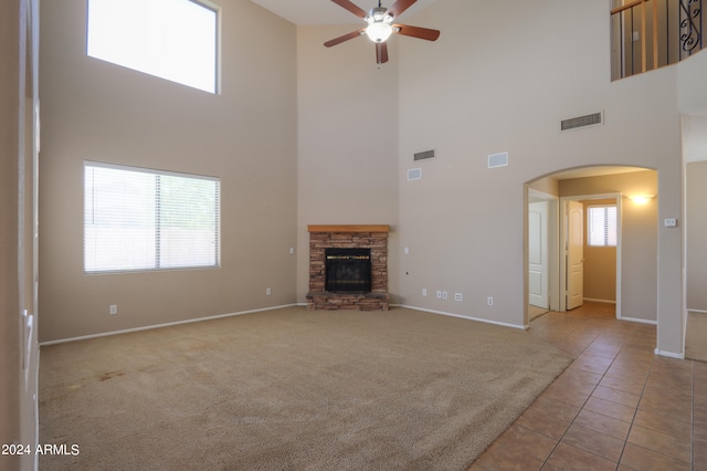 unfurnished living room featuring a stone fireplace, light carpet, and a high ceiling