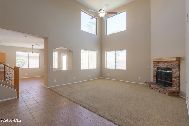 unfurnished living room with light carpet, a towering ceiling, a stone fireplace, and a wealth of natural light