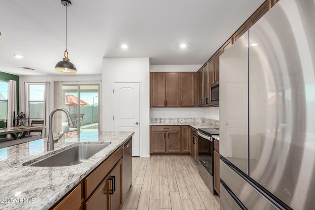 kitchen featuring appliances with stainless steel finishes, sink, hanging light fixtures, light stone counters, and light hardwood / wood-style floors