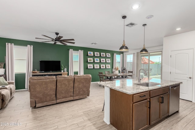 kitchen featuring decorative light fixtures, an island with sink, sink, ceiling fan, and light stone counters