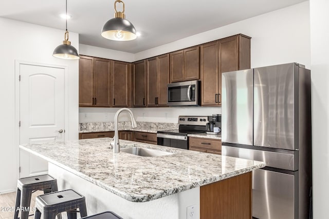 kitchen with appliances with stainless steel finishes, an island with sink, sink, hanging light fixtures, and light stone countertops