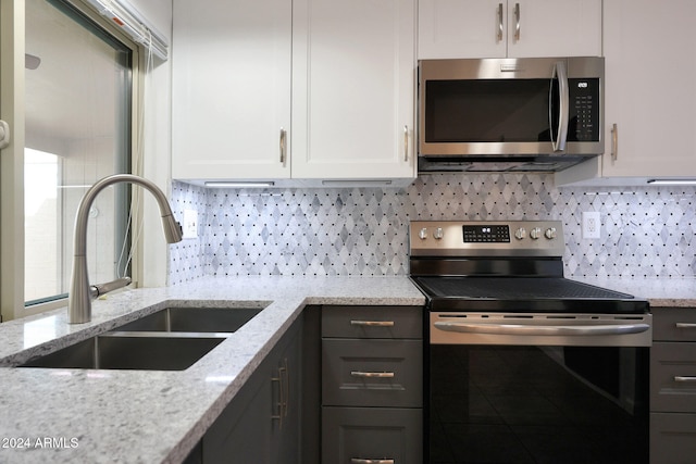 kitchen with light stone countertops, appliances with stainless steel finishes, white cabinetry, and sink