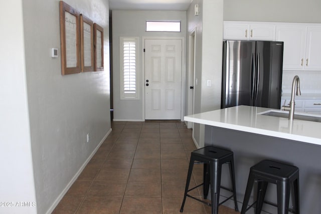 kitchen featuring a breakfast bar, sink, white cabinetry, stainless steel refrigerator, and dark tile patterned floors