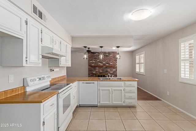 kitchen featuring visible vents, a sink, a peninsula, under cabinet range hood, and white appliances